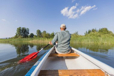 Genç bir adam dağ gölünde bir kanoda kürek çekiyor, yaz güneşinin tadını çıkarıyor. Doğa kaçış kavramları.