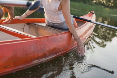 Genç bir kadın, sakin bir gölde kanoya binip yeşil doğal ortamın tadını çıkarırken dinleniyor. Kano konsepti.