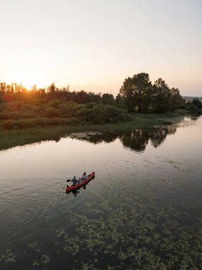 Gün batımında kano süren bir çift, akşamları güzel bir gölde kano süren iki siluet, havadan çekim. Doğa zevki ve rahatlama kavramları.