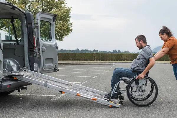 stock image Female assistant pushing a man with disability, a wheelchair user up the car ramp into the van. Accessibility and travel concepts.