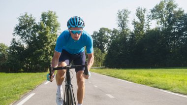 Kaslı bir adam, profesyonel bir yarış bisikletçisi, hızlı bisiklet sürüyor, poposu eyerden kalkık ve pedal çeviriyor.