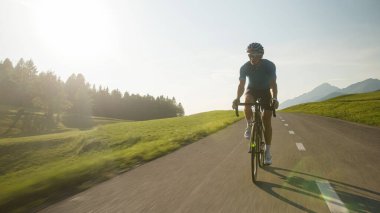Kaslı bir adam, profesyonel bir yarış bisikletçisi, hızlı bisiklet sürüyor, poposu eyerden kalkık ve pedal çeviriyor.