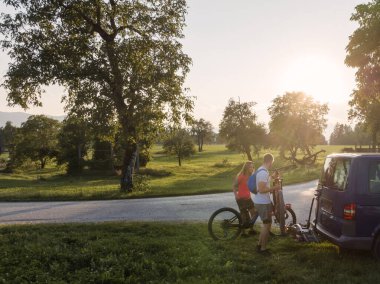 Genç bir adam ve bir kadın off-road bisikletine hazırlanıyor, karavanın bisiklet parkından elektrikli dağ bisikletlerini indiriyorlar..
