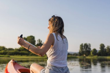 Genç bir kadın, sakin bir gölde kanoya binip yeşil doğal ortamın tadını çıkarırken dinleniyor. Kano konsepti.