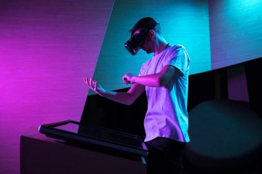 VR kulaklıklı genç adam mor ışıklı bir odada sanal gerçeklik deneyimi yaşıyor, havada çeşitli el hareketleri yapıyor..