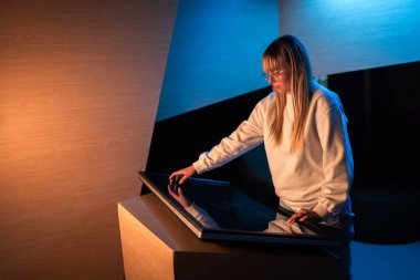 Dokunmatik ekranı kullanan ergen bir kız modern müze sergisindeki etkileşimli içeriği ustalıkla arıyor. Dijital teknoloji kavramı.