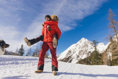 Erkek, karlı dağ bölgesinde kız arkadaşını köpeğiyle birlikte sırtında taşır.