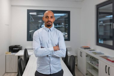 Kollarını kavuşturup, portre fotoğrafı çektirmiş, gururla poz veren kendinden emin, Afro-Amerikan bir adam. İş kavramlarında profesyonellik ve uzmanlık.