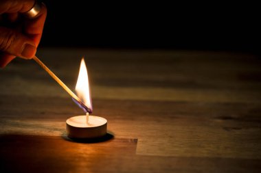 Erkek el ahşap bir masada küçük beyaz bir çay mumu yakıyor, yakın çekim. Tealight ambians konsepti.