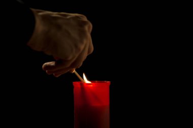 Male hand, using a safety match, lighting a red cemetery candle, on a black background, close up shot. All saints day concept. clipart