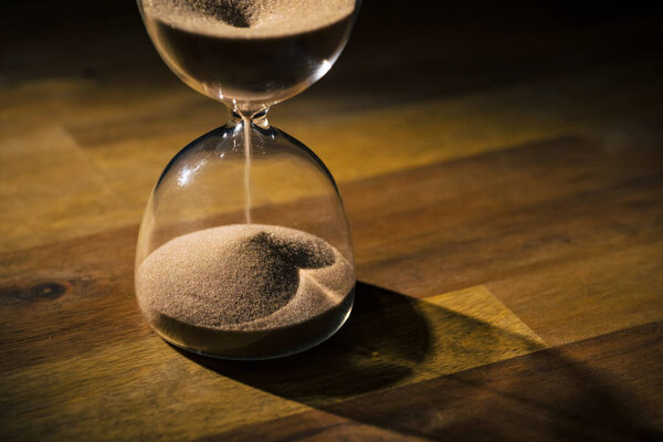 Hourglass on a wooden table with a black background, sand flowing through the bulb. Time, and life journey concepts.