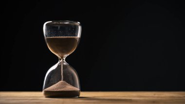 Siyah arka planda kum saati, akan altın kum taneleri yığının üzerine düşüyor, yakın çekim. Değişim, kararsızlık ve geçicilik kavramları.