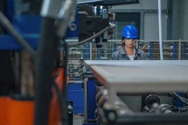 Mavi kasklı ve güvenlik gözlüklü Hintli kadın mühendis, kontrol panelini çalıştırıyor, endüstriyel işlemleri kontrol ediyor ve otomatikleştiriyor..