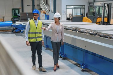 Hintli kadın fabrika yöneticisi, iş başında mavi kasklı ve sarı yelekli Afrikalı bir erkek çalışanı makineleri çalıştırması için eğitiyor..