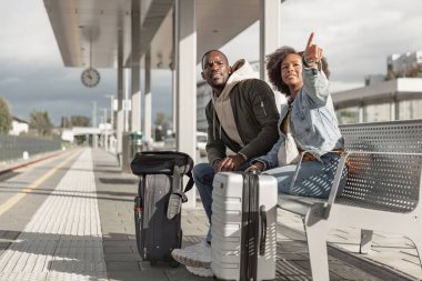 Gülümseyen yolcular, tren istasyonuna ulaşmayı bekleyen bir çift yaklaşan yolculukları için heyecanlı..