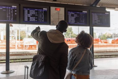 Afrika kökenli Amerikalı bir çift tren istasyonunda varış zamanını kontrol ediyor. Bilgi, ulaşım ve turizm kavramları.