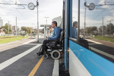 Elektrikli sandalyede engelli bir adam trene biniyor. Erişilebilir seyahat ve kapsayıcı ulaşım kavramları.