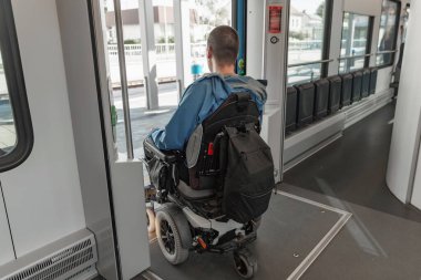 Elektrikli sandalyedeki engelli bir adam trenden çıkıyor. Erişilebilir seyahat ve kapsayıcı ulaşım kavramları.