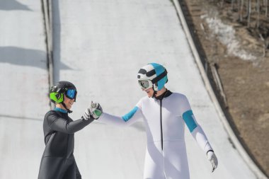 Two happy male ski jumpers giving high five in the outrun at a training on snow. clipart