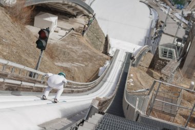 Ski jumper sitting on a start bar on top of ski jump focusing on speeding up down the inrun track. Winter sports concept. clipart