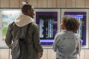 Afrika kökenli Amerikalı bir çift tren istasyonunda varış zamanını kontrol ediyor. Bilgi, ulaşım ve turizm kavramları.