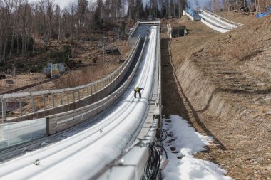 Ski jumper sitting on a start bar on top of ski jump focusing on speeding up down the inrun track. Winter sports concept. clipart