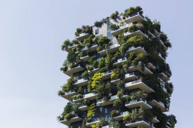 Konut kulesi, çeşitli bitkiler ve ağaçlarla kaplı balkonları olan modern mimarinin bir örneği. Sürdürülebilirlik ve ağaç gökdelen kavramı.