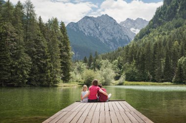 Anne rıhtımda oturmuş çocuklarını, kızını ve oğlunu kucaklıyor görkemli dağ ve göl manzarasının tadını çıkarıyor. Aile zamanı ve tatil kavramları.