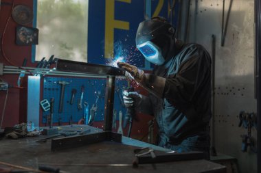 Bir atölyedeki tehlikeli kaynak işlemi sırasında deneyimli ve yetenekli bir kaynakçı. İş yeri, sağlık ve güvenlik kavramları.