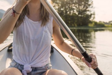 Genç bir kadın, sakin bir gölde kanoya binip yeşil doğal ortamın tadını çıkarırken dinleniyor. Kano konsepti.