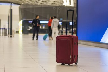 Havaalanı terminalinde kırmızı-kahverengi seyahat valizi ve arka planda bulanık yolcular. Seyahat, bagaj ve havacılık kavramları.