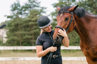 Siyah kasklı bir kadın kestane rengi at kafasını okşuyor, yakın çekim. İnsan ve hayvan ilişkileri kavramı.