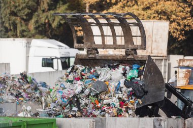 Yellow skid steer loader moving wooden waste material, shaking out a scrap grapple on the garbage heap in the materials recovery facility