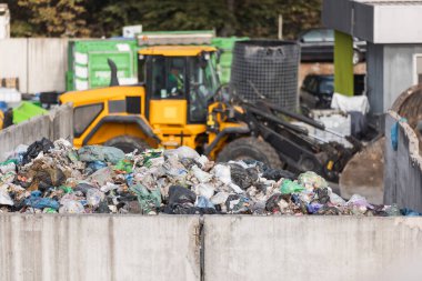 Yellow skid steer loader moving wooden waste material, shaking out a scrap grapple on the garbage heap in the materials recovery facility