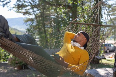 Afro-Amerikalı bir adam doğayı seviyor, bir hamakta sallanıyor ve dinleniyor kulaklıkla müzik dinliyor..