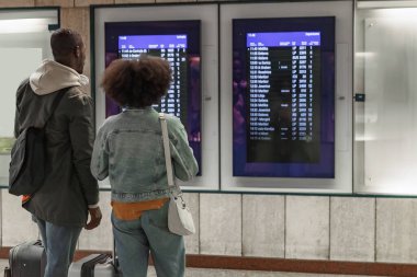 İki yolcu, bir Afro-Amerikan çift bir tren istasyonundaki kalkış tahtasına bakıyor. Seyahat ve turizm kavramları.