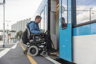 Elektrikli sandalyede engelli bir adam trene biniyor. Erişilebilir seyahat ve kapsayıcı ulaşım kavramları.