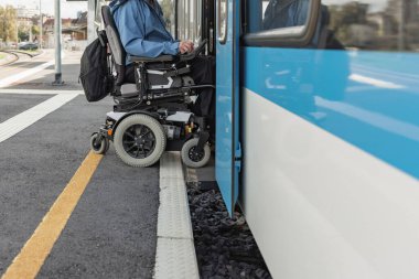 Elektrikli sandalyede engelli bir adam trene biniyor. Erişilebilir seyahat ve kapsayıcı ulaşım kavramları.
