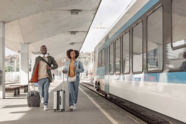 Tren istasyonunda yürüyen ve bavullarını taşıyan Afro-Amerikalı çift tren yolculukları için hazırlar. Gezgin yaşam tarzı konsepti.