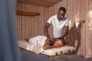 Profesyonel Afrikalı Amerikalı masör, lüks bir tatil köyü konuğu olan bayan müşteriye rahatlatıcı bir masaj yapıyor..