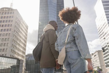 Afrikalı Amerikalı turist, şehir merkezindeki modern otel gökdelenine giderken bavullarını şehir caddesinde yuvarlıyor..