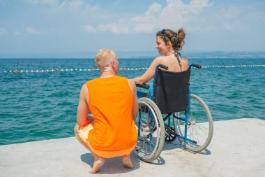 Tekerlekli sandalyedeki engelli kadın cankurtaran yardımıyla deniz kenarında tatilin tadını çıkarıyor.