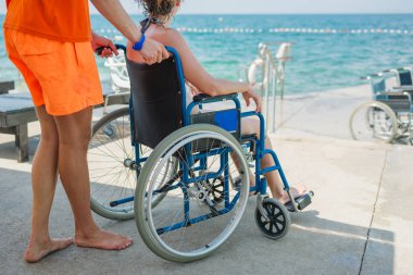 Tekerlekli sandalyedeki engelli kadın cankurtaran yardımıyla deniz kenarında tatilin tadını çıkarıyor.