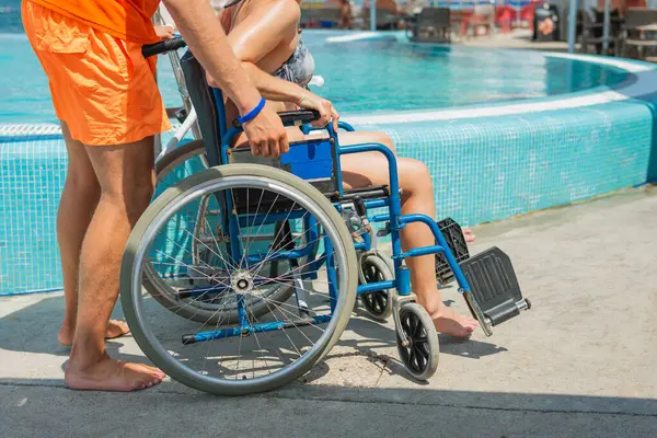 Deniz oteli cankurtaranı engelli bir kadına yardım ediyor erişilebilir hizmetler ve tesisler, havuz sandalyesi kaldırma, ve tekerlekli sandalye, tatil köyünde..