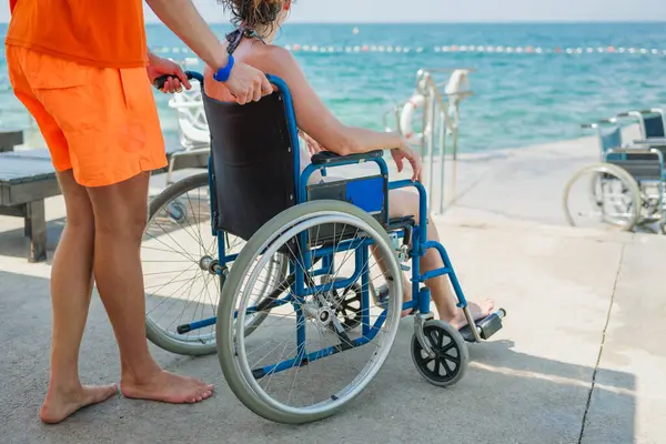 Tekerlekli sandalyedeki engelli kadın cankurtaran yardımıyla deniz kenarında tatilin tadını çıkarıyor.