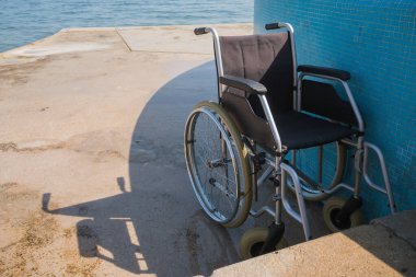 Engelliler için boş mavi çelikli tekerlekli sandalye, deniz kenarına yerleştirilir, güzel sahil çevresine erişim sağlanır..