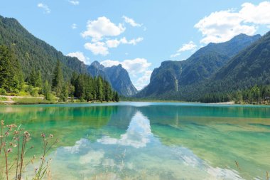 İtalya 'daki görkemli Dolomite dağlarına karşı hazırlanan Toblacher See, açık mavi gökyüzü altında, tüylü bulutlar altında, doğa aşıkları ve fotoğrafçılar için mükemmel turkuaz suları sergiliyor..
