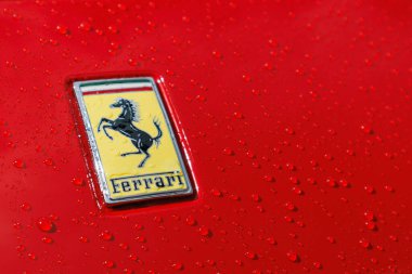 Slovenya, Ljubljana - 16 Mayıs 2025: Islak yüzeyde su damlacıkları ile kırmızı Ferrari lüks spor otomobil logosu