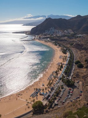 Playa de Las Teresitas 'ın nefes kesici manzarası, açık mavi gökyüzünün altında altın kumlar, palmiye ağaçları ve parıldayan sular sergileniyor. Canlı plaj, rahatlamak ve keyif almak için ziyaretçileri cezbediyor..