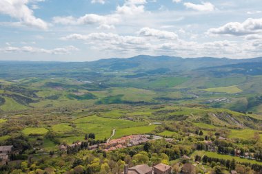 Açık gökyüzünün altındaki Toskana 'nın yuvarlanan tepelerinin nefes kesici manzarası. Aşağıdaki yeşil alanlar, tuhaf köylerle dolu. Manzara, baharda İtalyan kırsalının güzelliğini gözler önüne seriyor..